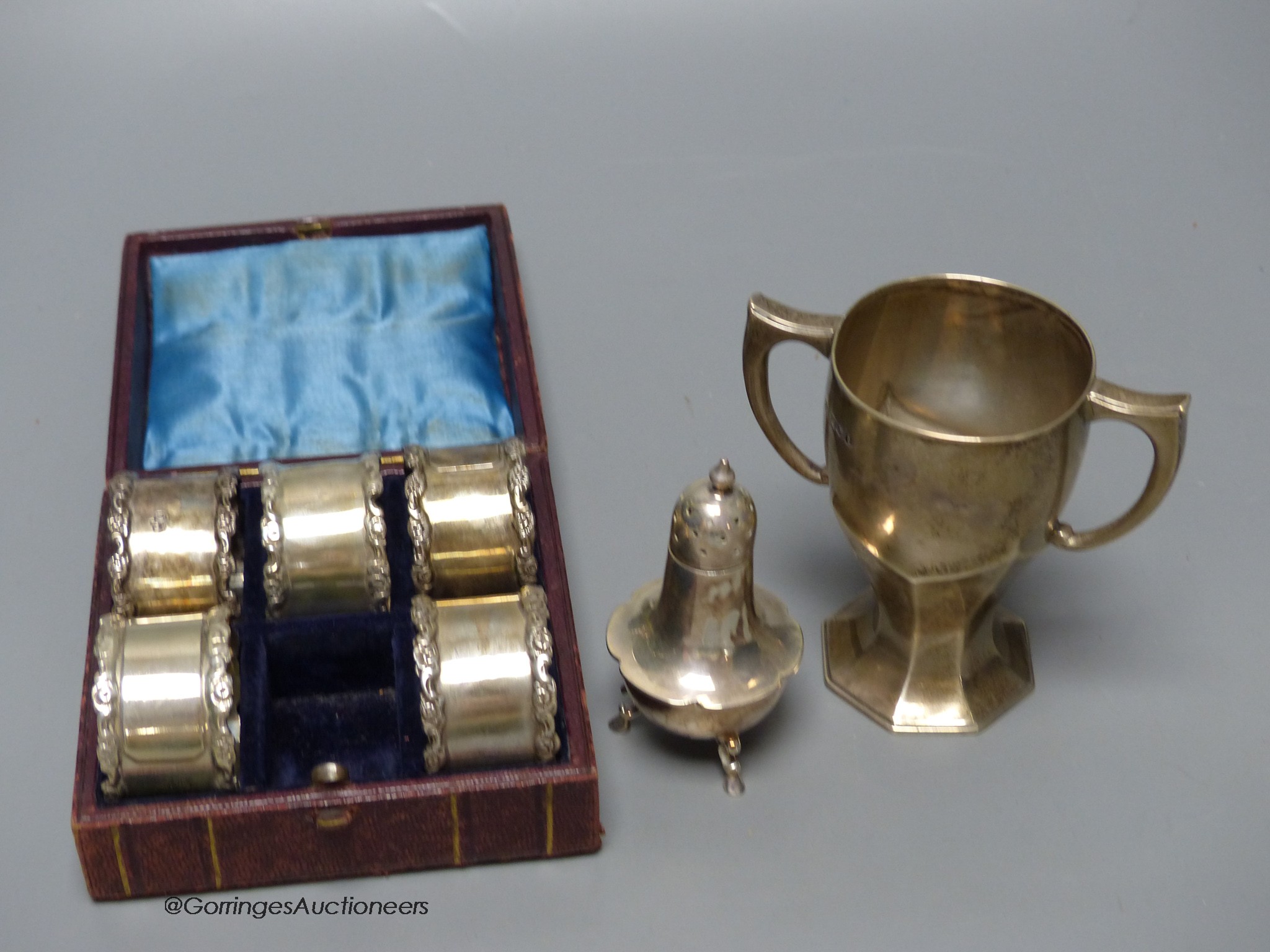 A Mappin & Webb small silver trophy cup, a silver pepperette and five cased silver napkin rings.